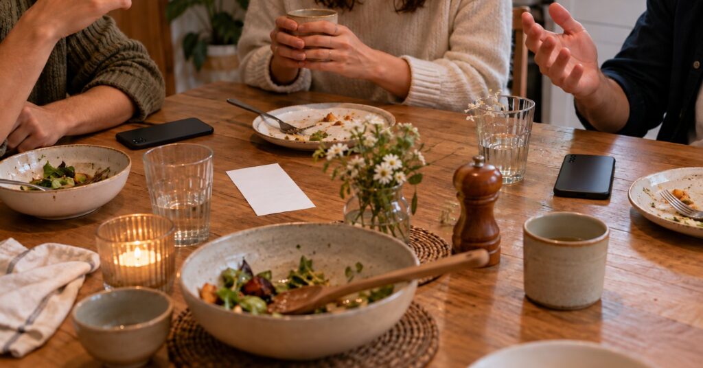 Friends at a kitchen table after a meal, phones face down and a receipt turned over.